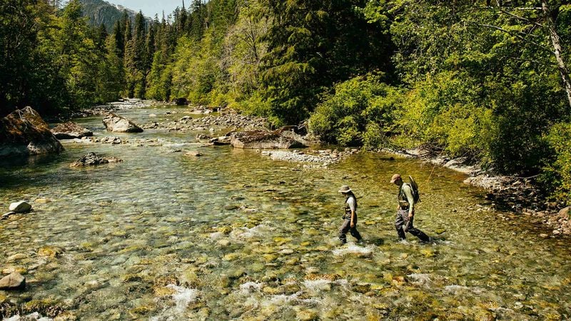 Two people in fly fishing gear crossing a shallow river