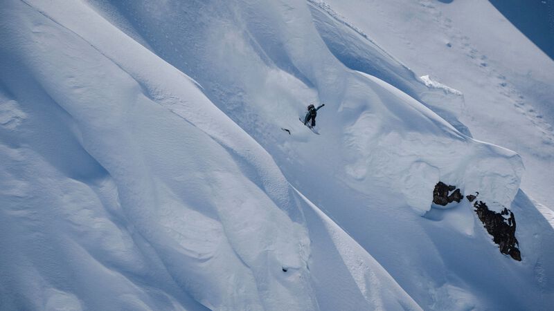 A snowboarder catches air on a big mountain route.