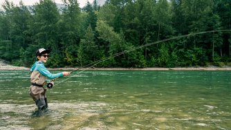 Un enfant sourit en tenant une canne &agrave; mouche dans une rivi&egrave;re.